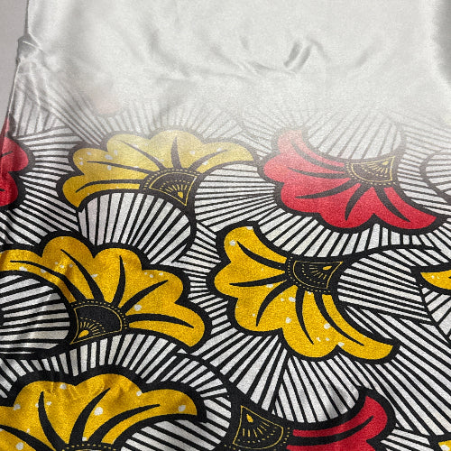 Close-up of a fabric with a floral pattern featuring red, yellow, and black colors on a white background.