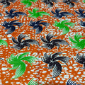 Patterned fabric with black, green, and white designs on an orange background