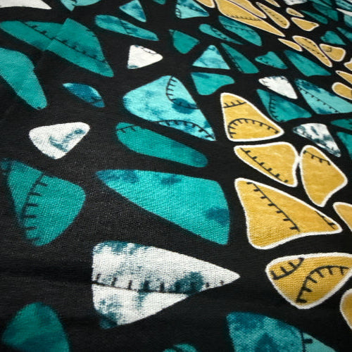 Close-up of fabric with geometric pattern featuring triangles in teal, yellow, and white on a black background.