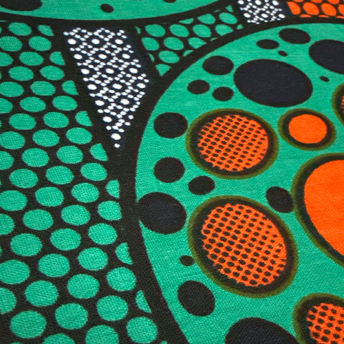 Close-up of a fabric with colorful abstract patterns in green, orange, black, and white.