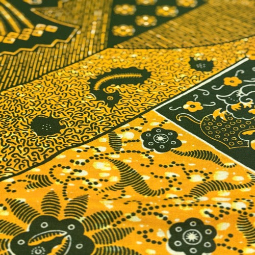Close-up of a patterned fabric with black and gold designs on a yellow background