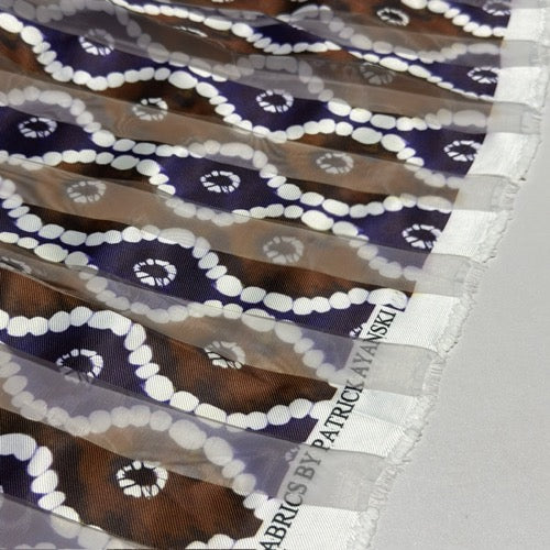 Close-up of patterned fabric with a visible label, featuring shades of purple, white, and brown.